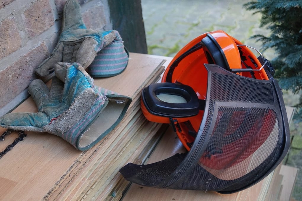 Well-worn work gloves beside a helmet with ear defenders and a face visor.