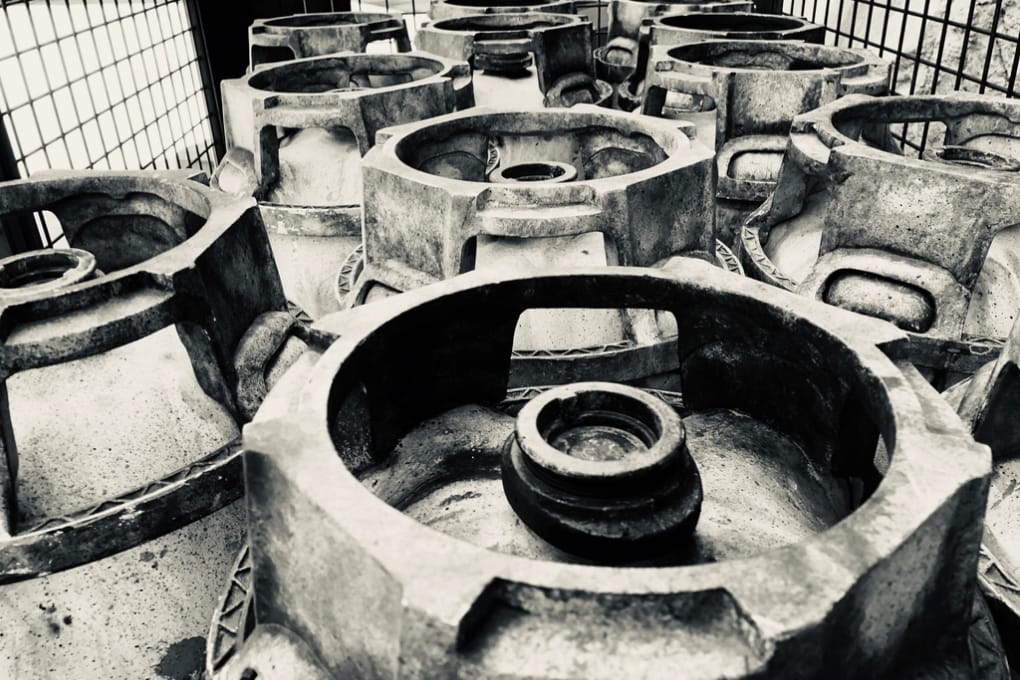 Cast metal housings stacked and held behind a wire cage, awaiting disposition.