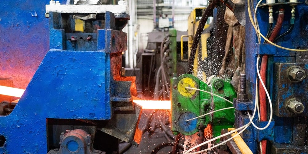 A hot rolling line with a glowing steel bar running between mill stands.