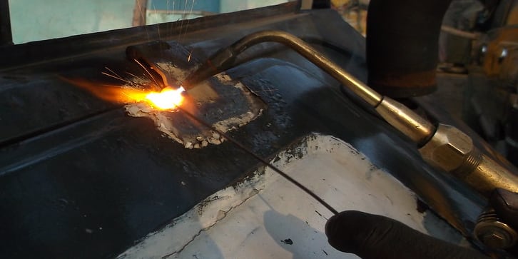 A cutting torch working a steel panel, sparks coming off the weld pool.