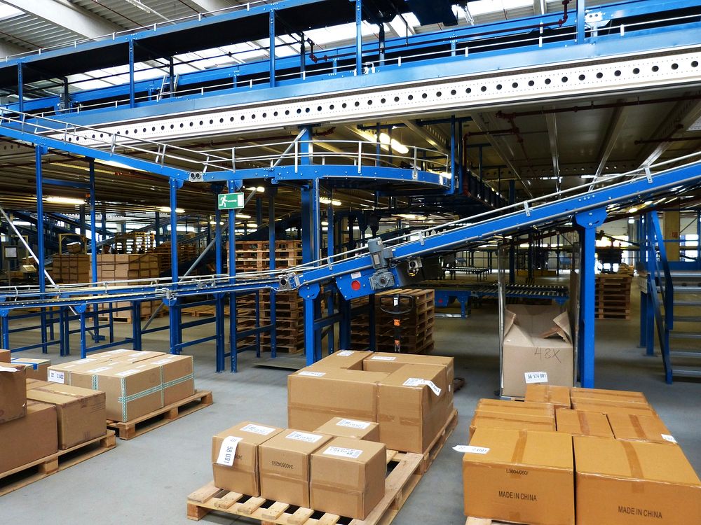 Conveyor lines running through a material-handling facility with palletised and boxed stock staged alongside.