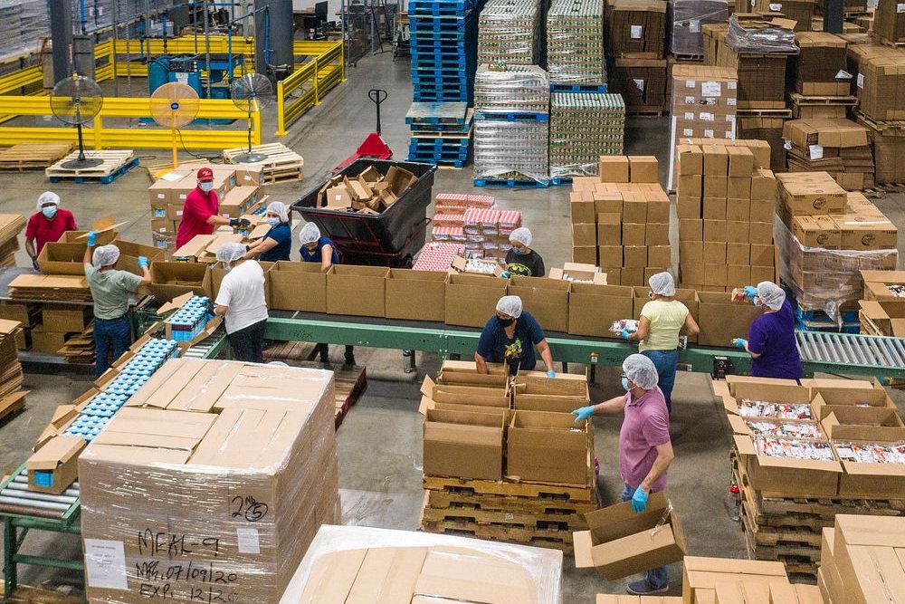 A full crew working a packing line across a production floor, each station staffed.