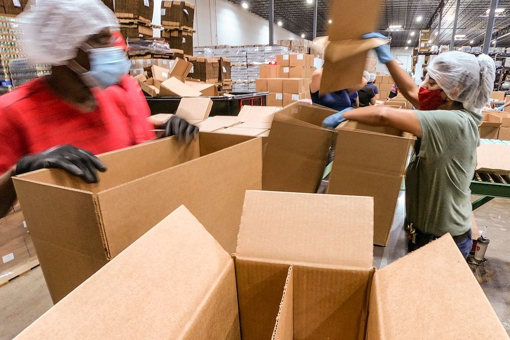 A warehouse crew opening and filling cartons beside staged pallets during a volume surge.
